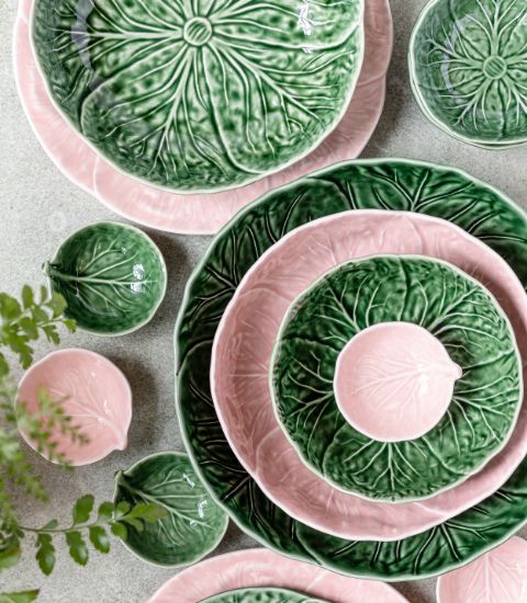 Ensemble d’assiettes et de bols en céramique émaillée, décorés en forme de feuilles vertes et roses, disposés en composition harmonieuse sur une table.