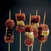 Brochettes de chistorra grillée d'Embutidos Hortanco, présentées sur fond noir.