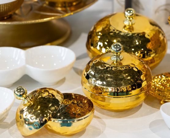 Set of round hammered golden metal boxes with knobbed lids, displayed on a table next to white bowls.