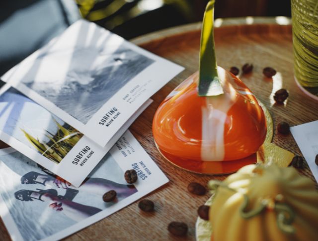 Close-up of a colorful dessert on a table, with surfing brochures and coffee beans scattered around.