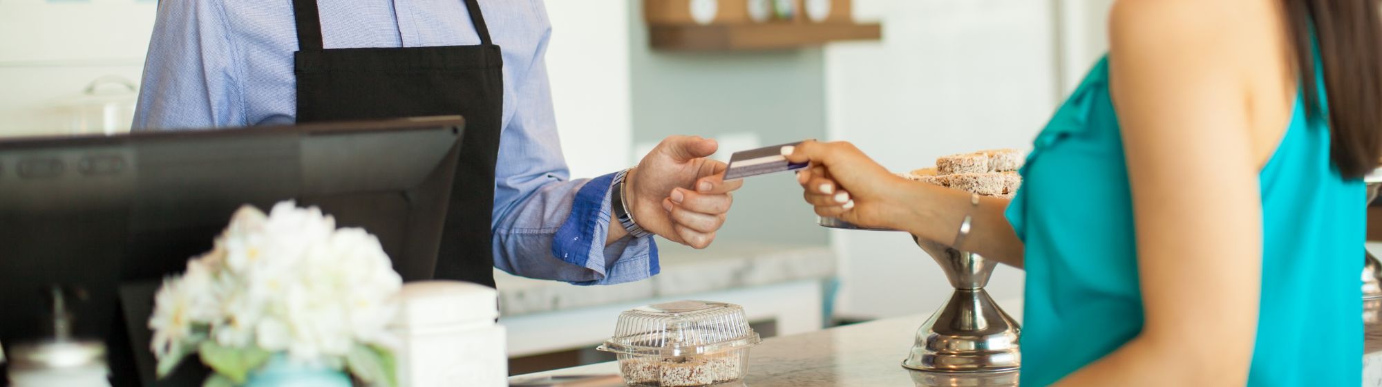 Client tendant une carte bancaire à un commerçant derrière un comptoir de boutique.