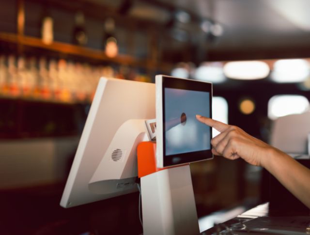 Hand using a touchscreen cash register in a modern bar or restaurant.