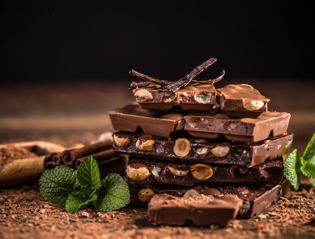 Stack of chocolate bars with whole hazelnuts, garnished with vanilla and fresh mint.
