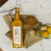Bouteille de jus de yuzu Alain Milliat posée sur un torchon avec fruits et céréales sur une table en marbre.