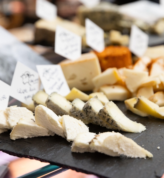 Assorted sliced cheeses displayed on a slate board with labels in a cheese shop.