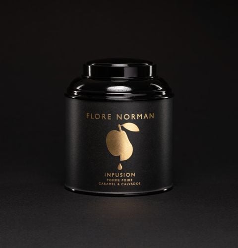 Black tin of apple pear caramel calvados infusion, photographed on an elegant black background.