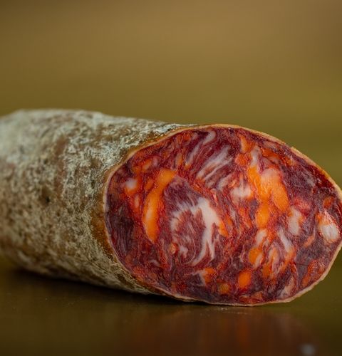 Saucisson sec tranché aux marbrures rouges et orangées, présenté en gros plan sur fond sombre.