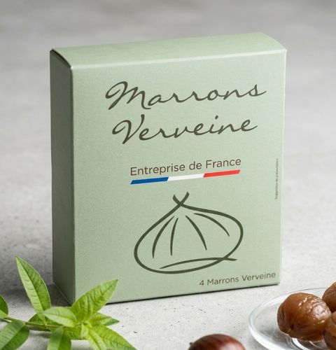 Boîte verte de marrons à la verveine, accompagnée de feuilles fraîches et de marrons glacés.