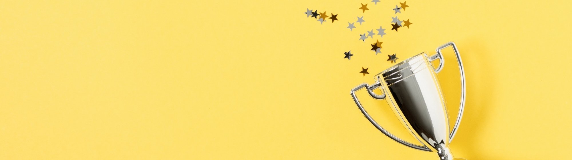 Large tilted silver trophy with star confetti on a panoramic yellow background.