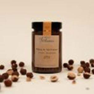 Jar of hazelnut spread surrounded by whole hazelnuts on a light beige background.