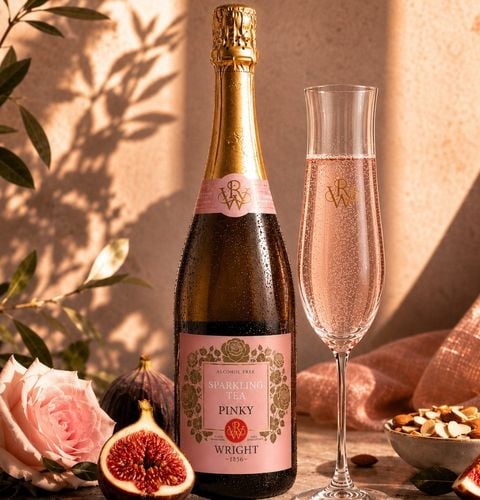 Bottle of alcohol-free sparkling rosé tea with a filled flute, surrounded by figs, almonds and a pink rose in soft light.
