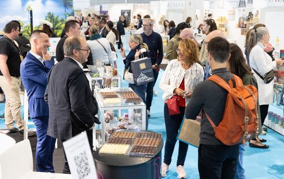 Visitors interacting at a trade show booth, with professionals discussing and engaging with various products on display, including chocolates and confectionery items